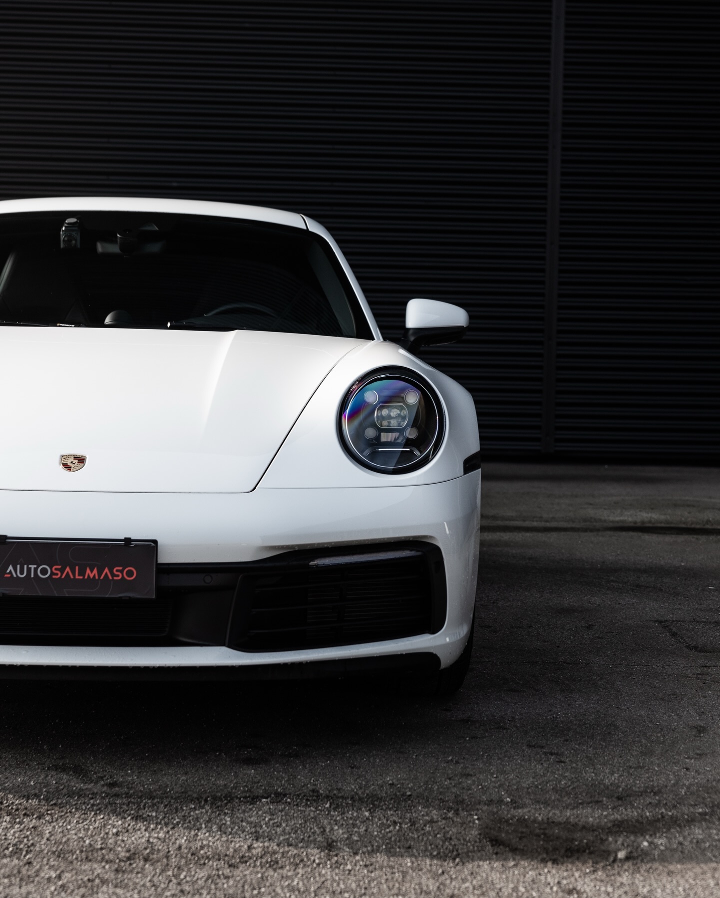 Frontale di Porsche 911 bianca con faro LED tondo, stemma sul cofano e targa AUTOSALMASO davanti a una parete nera